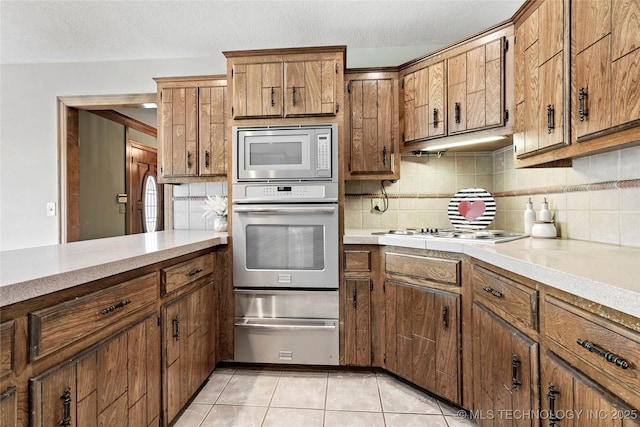 kitchen with appliances with stainless steel finishes, a warming drawer, brown cabinetry, light countertops, and a textured ceiling
