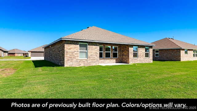 rear view of property with a yard, roof with shingles, brick siding, and a detached garage