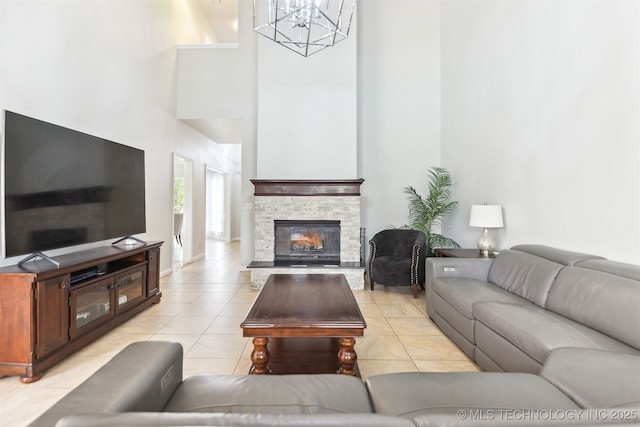 living area featuring a towering ceiling, a fireplace, a chandelier, light tile patterned floors, and baseboards