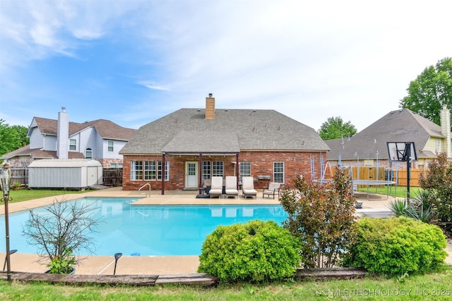 view of swimming pool with an outbuilding, a fenced in pool, a trampoline, a fenced backyard, and a storage unit