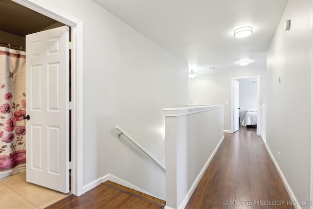 hallway featuring baseboards, an upstairs landing, and wood finished floors