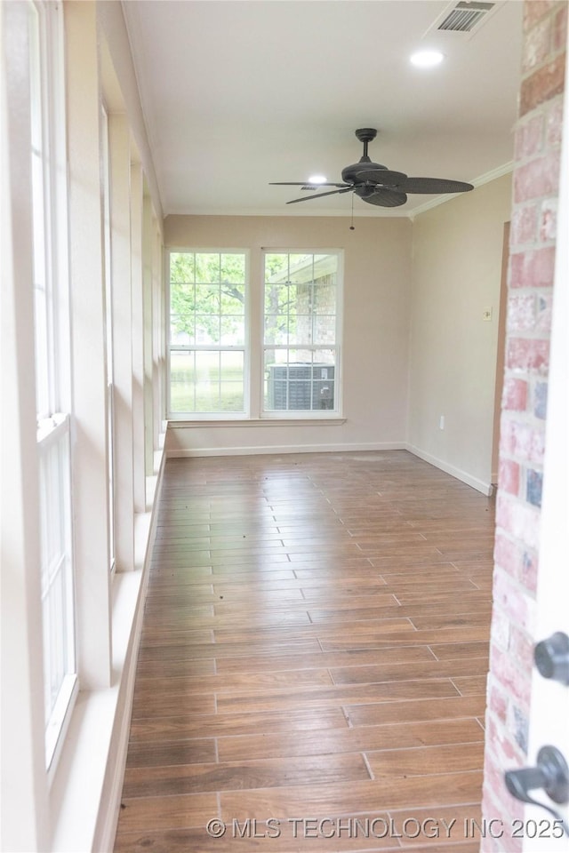 empty room featuring crown molding, wood finished floors, baseboards, and ceiling fan