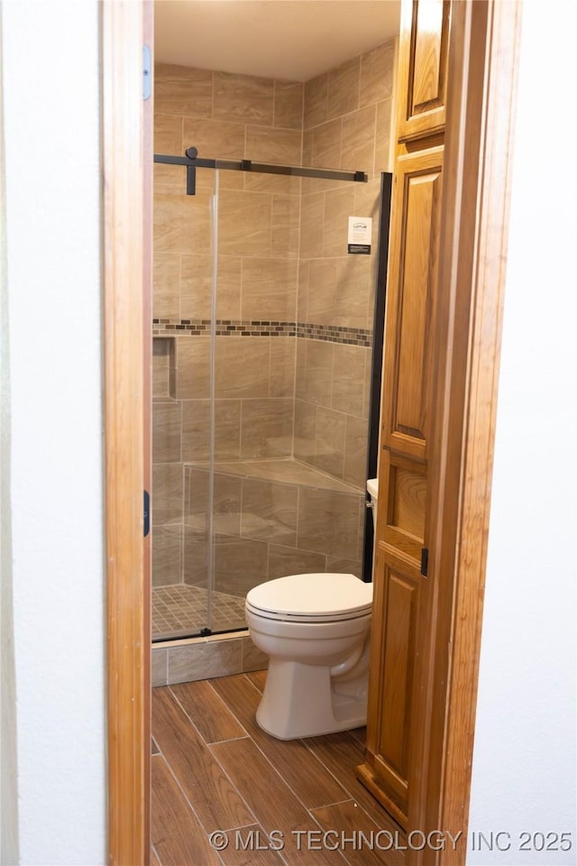 full bath featuring a stall shower, toilet, and wood finished floors