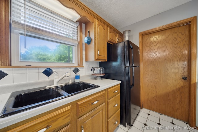 141 S Bryan St, Copan, OK 74022 - kitchen with brown cabinets, a sink, freestanding refrigerator, a textured ceiling, and light countertops