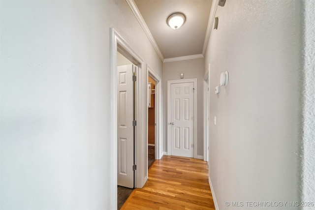 corridor with baseboards, ornamental molding, and light wood-style flooring