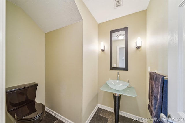 bathroom with baseboards, lofted ceiling, visible vents, and a sink