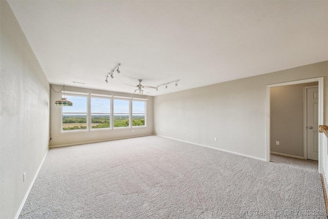 spare room featuring rail lighting, carpet flooring, and baseboards