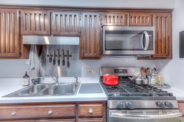 kitchen featuring light countertops, appliances with stainless steel finishes, brown cabinetry, and a sink