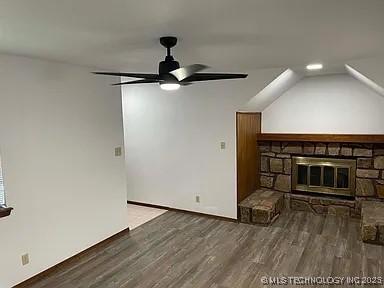 unfurnished living room featuring wood finished floors, vaulted ceiling, a ceiling fan, baseboards, and a stone fireplace