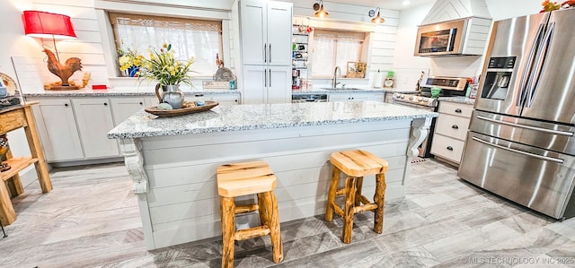 kitchen featuring light stone countertops, a sink, a kitchen bar, a kitchen island, and appliances with stainless steel finishes