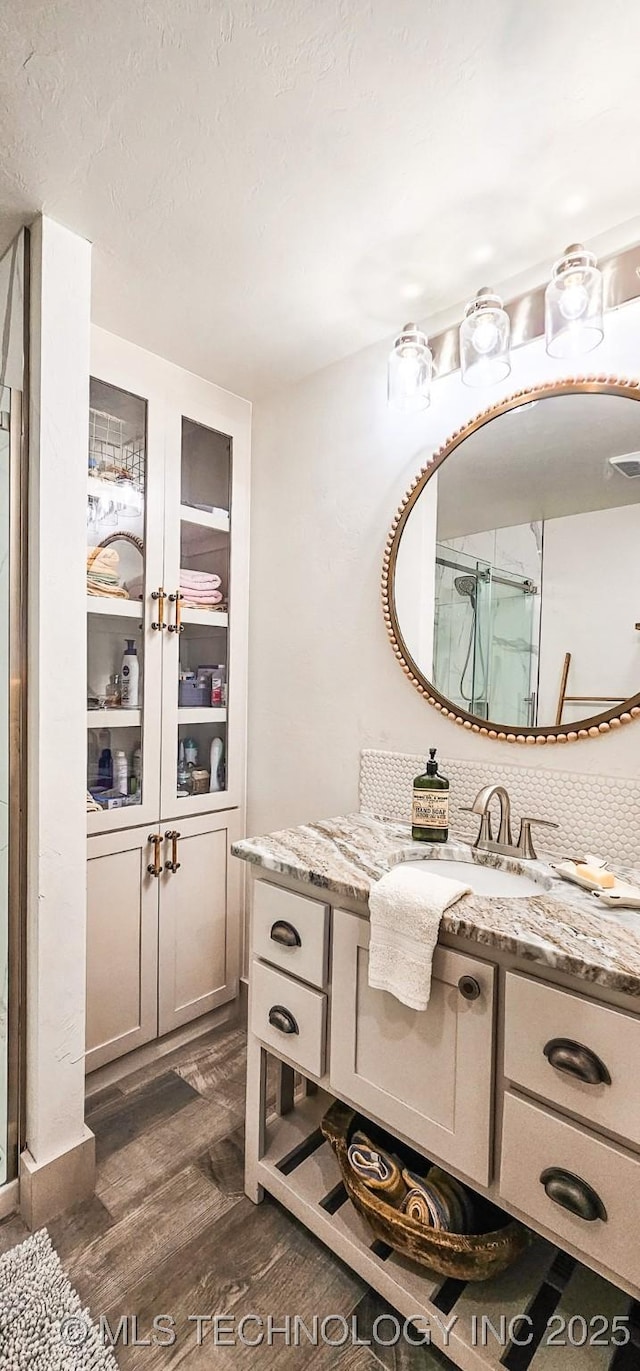 full bath featuring a shower with door, wood finished floors, vanity, and visible vents