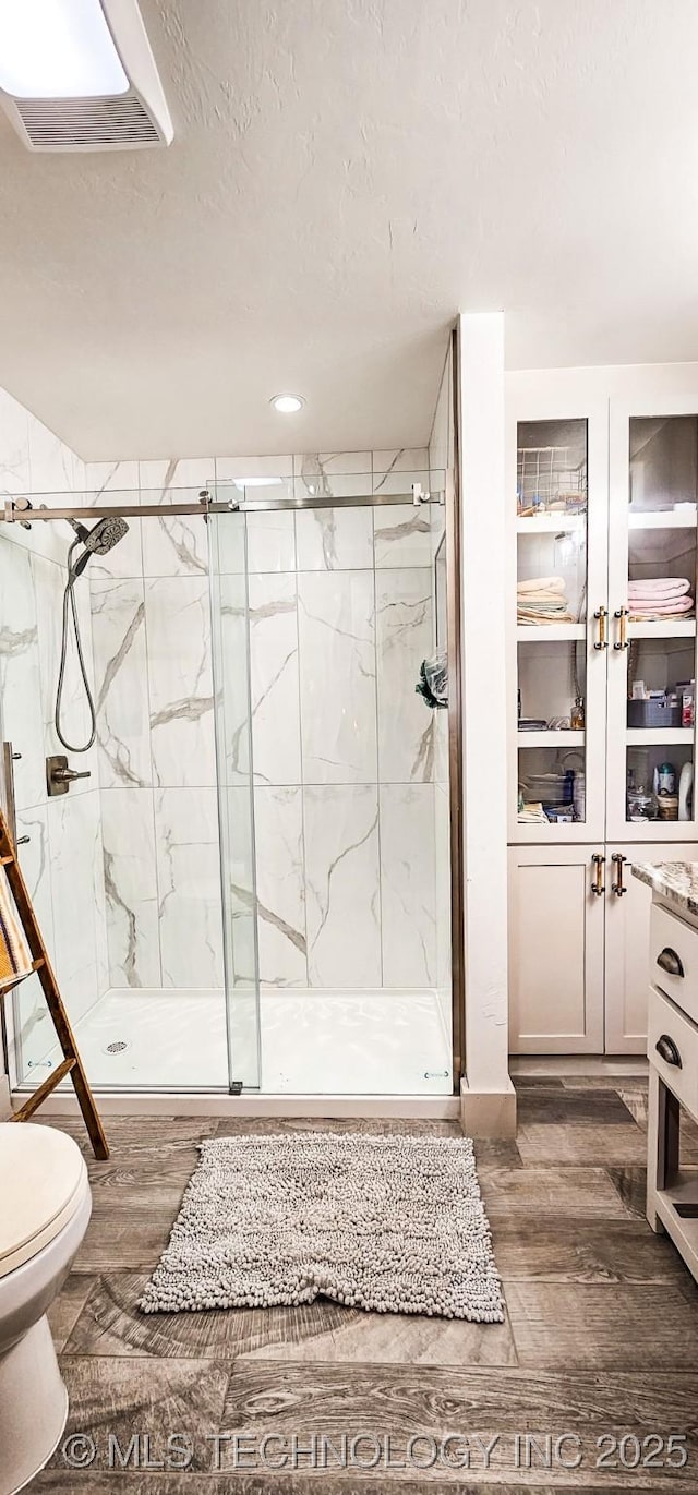 bathroom featuring a marble finish shower, visible vents, toilet, and wood finished floors