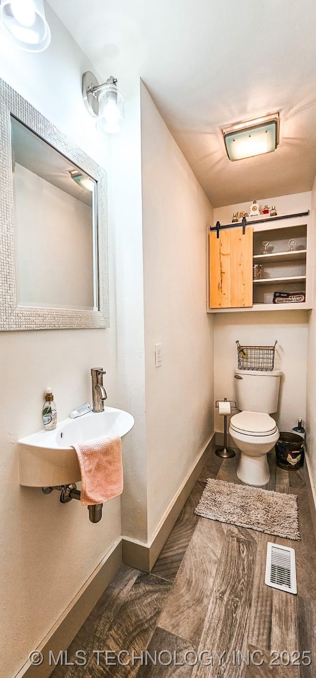 half bath featuring a sink, toilet, baseboards, and visible vents
