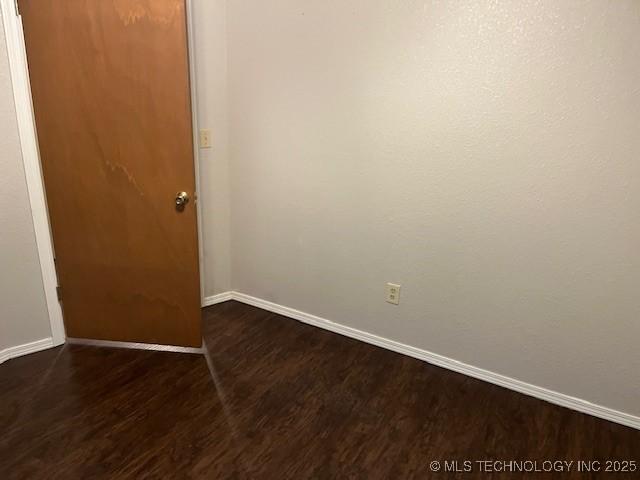 unfurnished room with baseboards and dark wood-type flooring