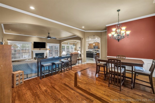 2501 Forest Ridge Parkway, Claremore, OK 74017 - dining space featuring arched walkways, ceiling fan, a chandelier, wood finished floors, and a glass covered fireplace