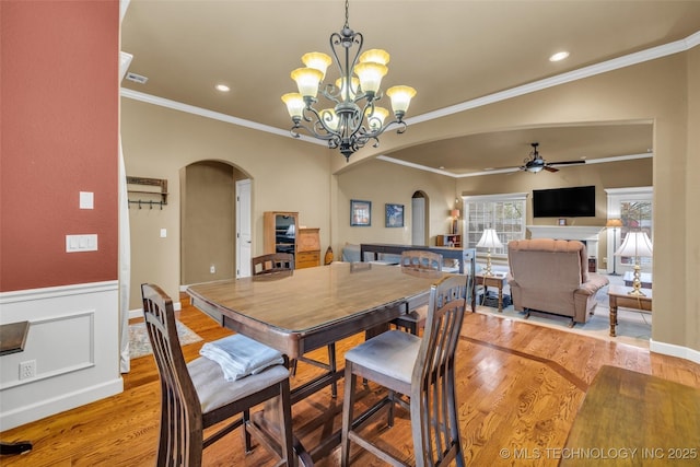 2501 Forest Ridge Parkway, Claremore, OK 74017 - dining room featuring arched walkways, wood finished floors, a ceiling fan, a chandelier, and a wainscoted wall