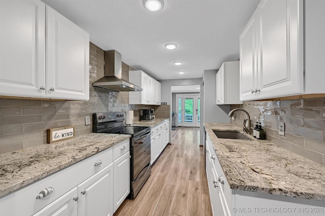 7626 Whispering Way, Kingston, OK 73439 - kitchen featuring a sink, light wood-type flooring, black electric range oven, wall chimney range hood, and decorative backsplash