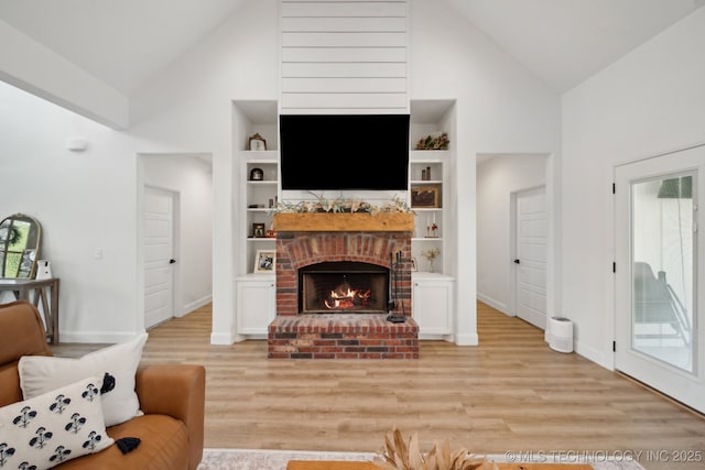 living area featuring baseboards, a fireplace, light wood-style flooring, and high vaulted ceiling