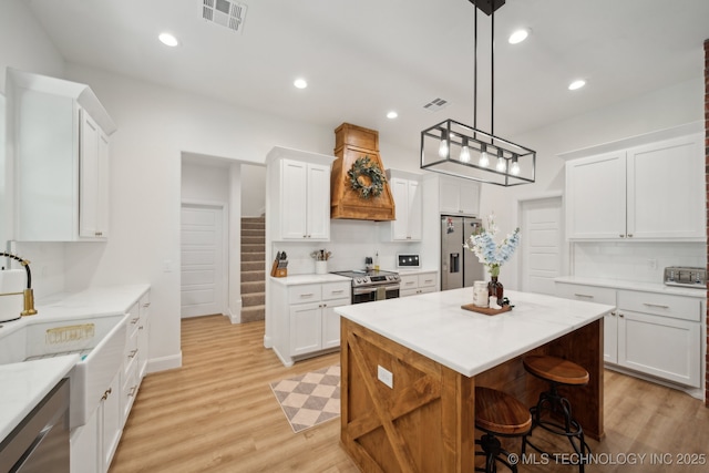 kitchen with premium range hood, stainless steel appliances, visible vents, white cabinets, and light wood-style floors