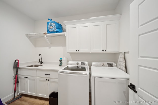 laundry room featuring a sink, light wood finished floors, cabinet space, and independent washer and dryer