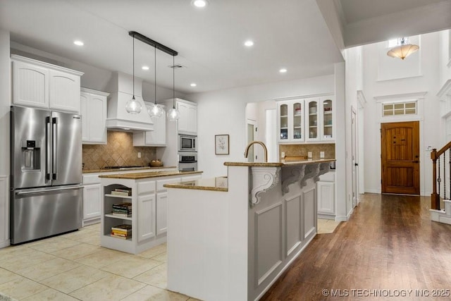 6811 S Sycamore Pl, Broken Arrow, OK 74011 - kitchen featuring appliances with stainless steel finishes, custom range hood, a center island with sink, decorative backsplash, and white cabinets