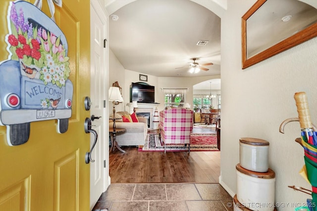 tiled entryway featuring ceiling fan, a glass covered fireplace, arched walkways, and a chandelier