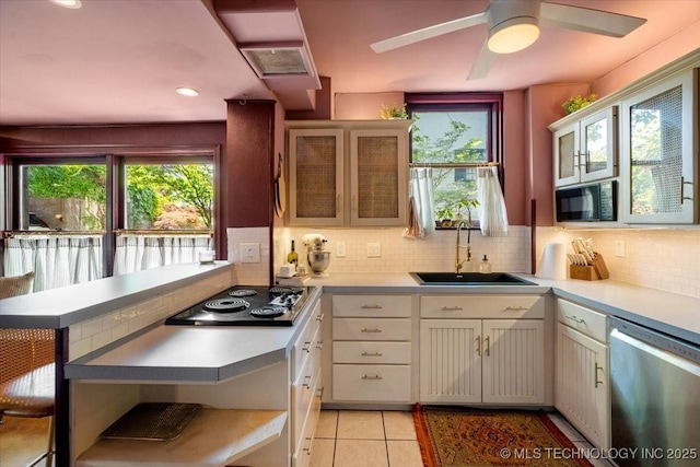 kitchen with a peninsula, a sink, electric cooktop, dishwasher, and black microwave