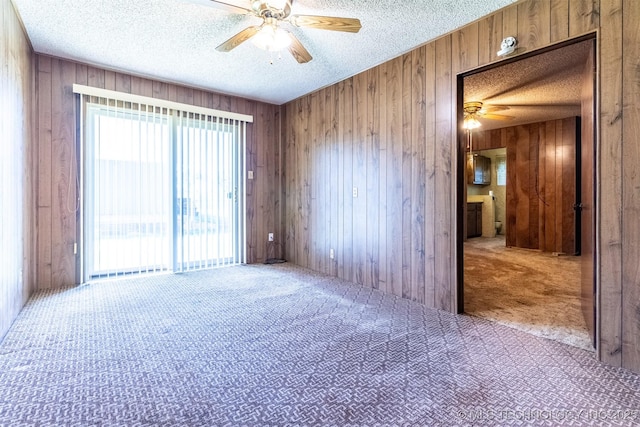 empty room with carpet flooring, wooden walls, ceiling fan, and a textured ceiling