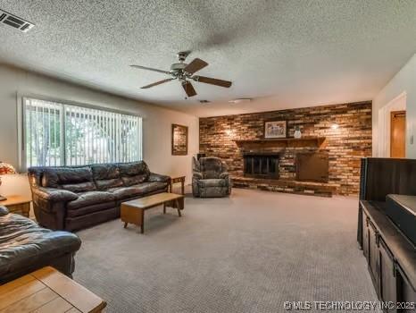 carpeted living area featuring ceiling fan, a brick fireplace, visible vents, and a textured ceiling