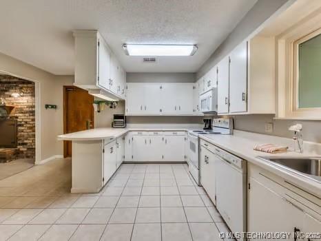 kitchen featuring a peninsula, light countertops, light tile patterned flooring, and white appliances