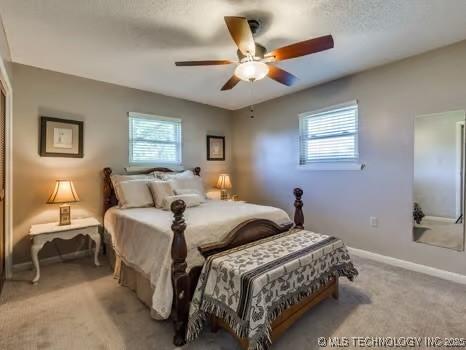 bedroom featuring multiple windows, light carpet, baseboards, and a ceiling fan