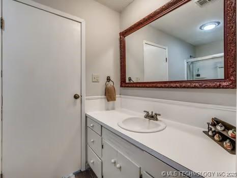 bathroom with a shower with shower door, vanity, and visible vents