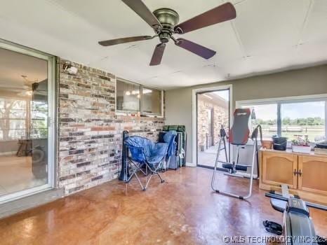 interior space with a ceiling fan and brick wall