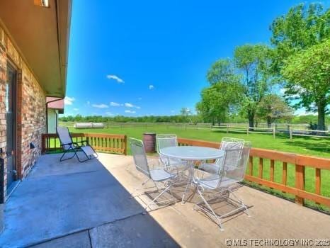 view of patio with outdoor dining area, fence, and a rural view