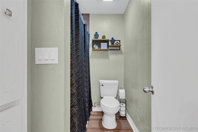 bathroom with wood finished floors, toilet, baseboards, and a textured wall
