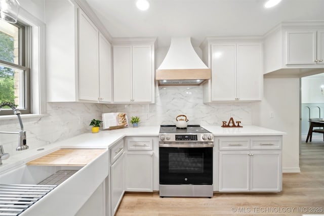 1402 E 125th St S, Jenks, OK 74037 - kitchen with stainless steel electric range oven, custom range hood, light wood-style floors, white cabinetry, and light countertops