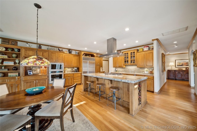 5263 Oak Leaf Dr, Tulsa, OK 74131 - kitchen featuring appliances with stainless steel finishes, island exhaust hood, ornamental molding, light wood-style floors, and backsplash