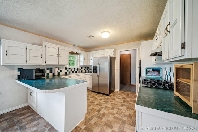 kitchen featuring stainless steel fridge, a peninsula, a sink, white cabinets, and decorative backsplash