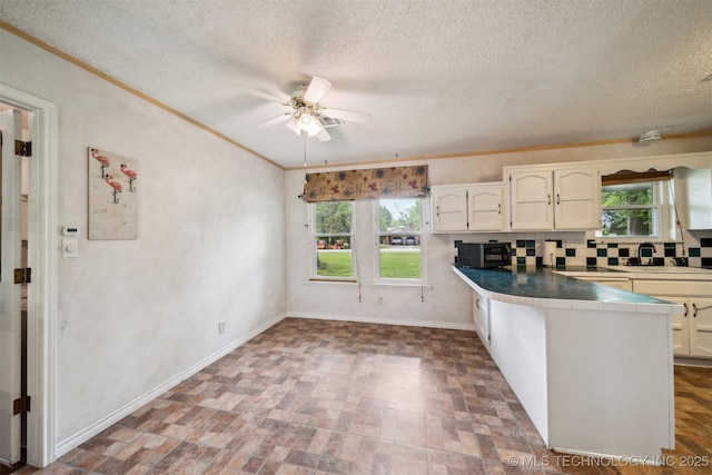 kitchen with black microwave, healthy amount of natural light, a ceiling fan, a peninsula, and a textured ceiling
