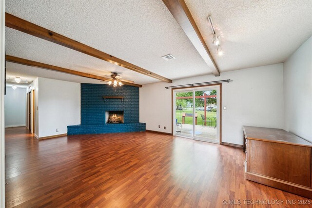 unfurnished living room featuring a textured ceiling, ceiling fan, beam ceiling, wood finished floors, and a brick fireplace