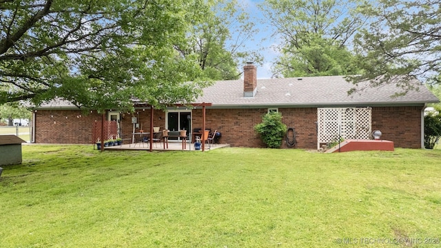 rear view of house with a patio, a yard, brick siding, a chimney, and a shingled roof