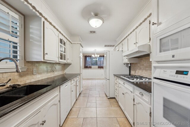 kitchen with white appliances, a sink, under cabinet range hood, dark countertops, and white cabinets