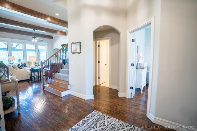 hallway featuring arched walkways, dark wood-type flooring, beamed ceiling, baseboards, and stairs