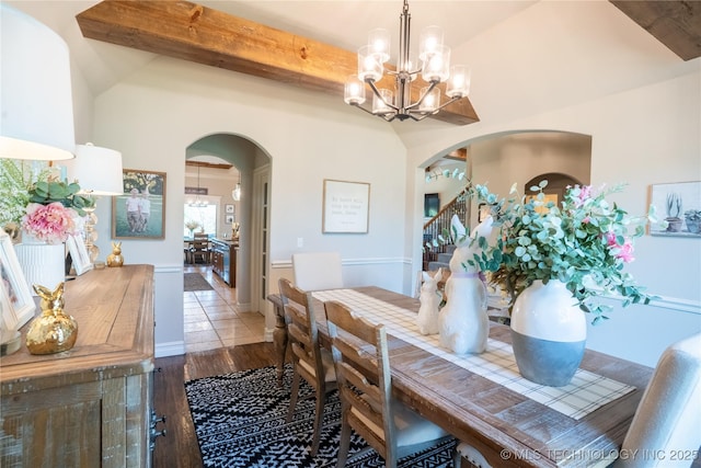 dining room with arched walkways, a chandelier, wood finished floors, beam ceiling, and stairway