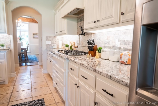 kitchen with stainless steel gas stovetop, fridge, tasteful backsplash, a chandelier, and range hood