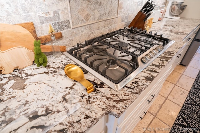 kitchen view of stainless steel gas cooktop, light stone countertops, and white cabinetry