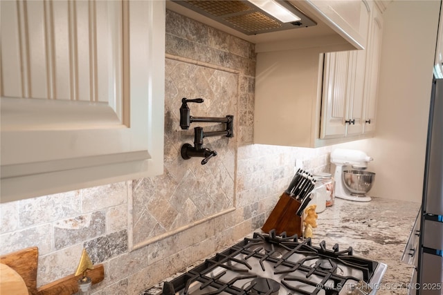 kitchen view of pot filler, light stone counters, tasteful backsplash, ventilation hood, and stainless steel gas cooktop