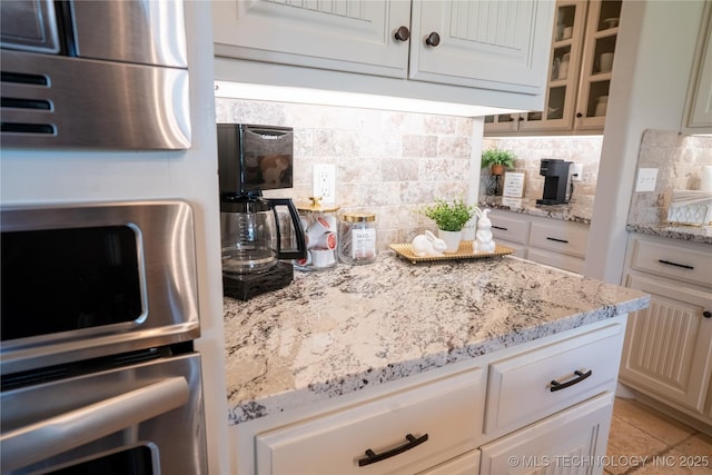 kitchen with glass insert cabinets, decorative backsplash, light stone counters, and wall oven