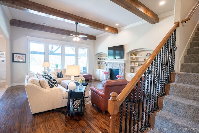living area with beamed ceiling, wood finished floors, baseboards, stairway, and a stone fireplace