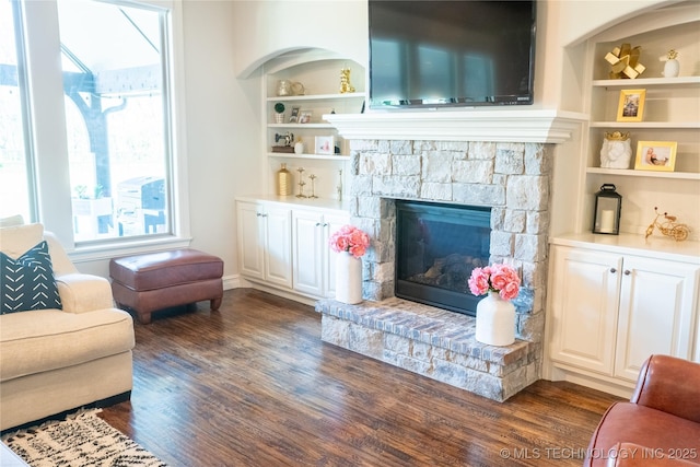 living area featuring dark wood-type flooring, built in features, and a fireplace